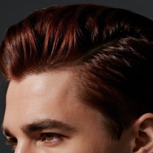 Man blow-drying hair with a round brush in a minimal bathroom, demonstrating directional hair styling techniques for men.