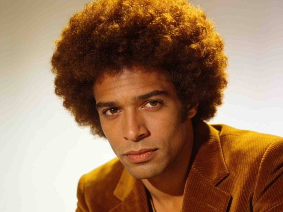 Man with a full rounded Afro wearing a mustard corduroy jacket.