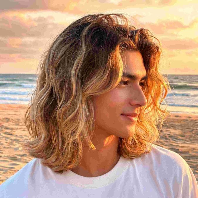 Man with sun-kissed shoulder-length surfer hair and loose beach waves.