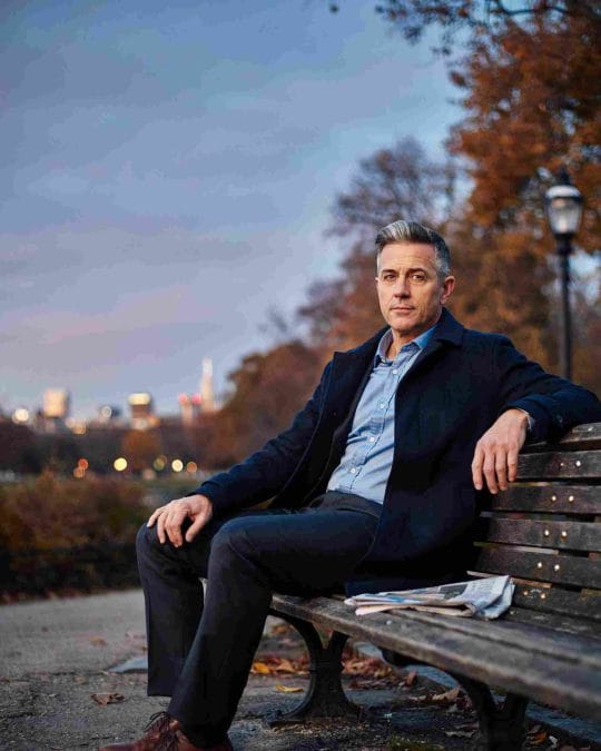 Man over 40 with an Ivy League haircut sitting on a park bench.