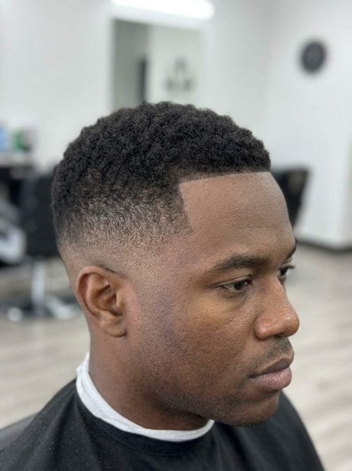 Low taper fade haircut with short natural curls and a crisp line up for a clean professional look.