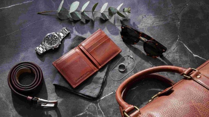Men’s accessories flat lay with watch, wallet, sunglasses, belt, jewelry, and leather bag.