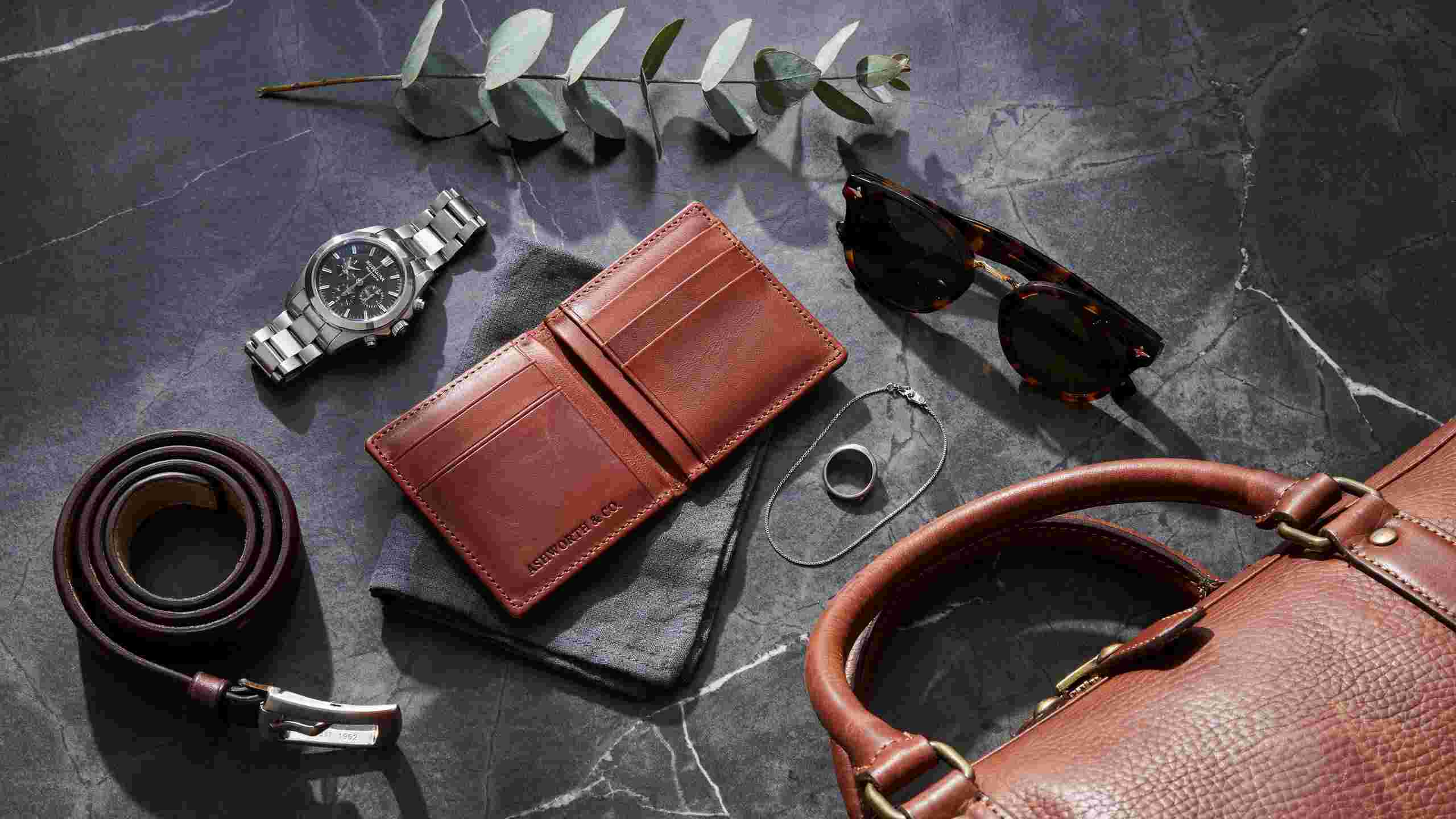 Men’s accessories flat lay with watch, wallet, sunglasses, belt, jewelry, and leather bag.