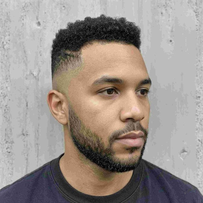 Man wearing a short Afro taper with compact coily texture, faded sides, and a shaped beard.
