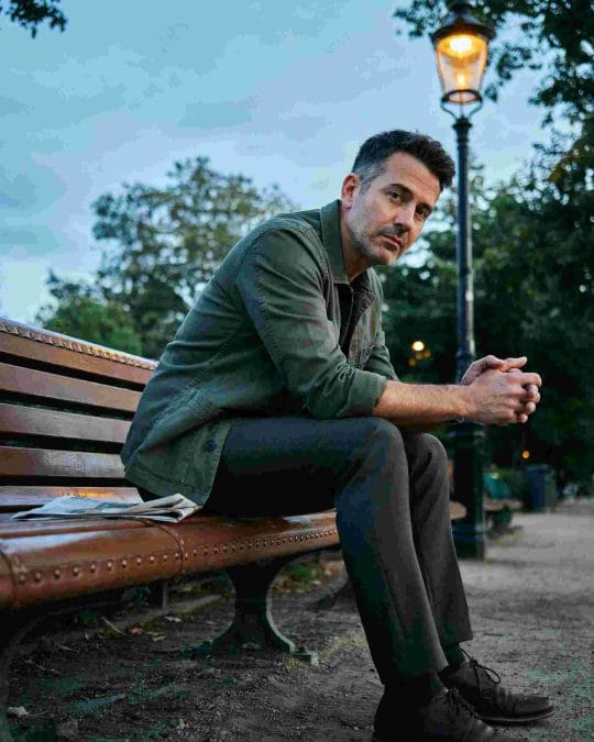 Mature man with a low fade and textured top sitting on a park bench.