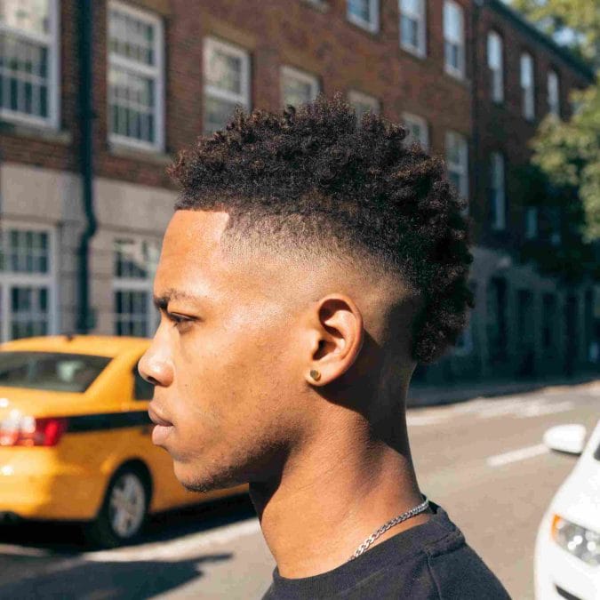 Mid fade haircut with curly textured hair on top, creating a balanced and modern profile.