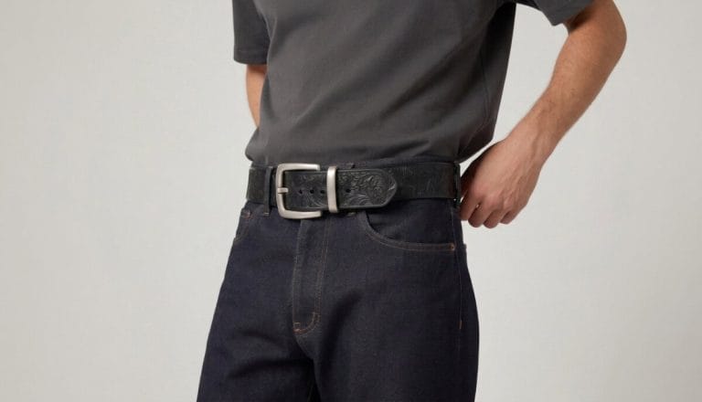 Man wearing a wide leather statement belt with a silver plaque buckle over dark jeans and a neutral tee.